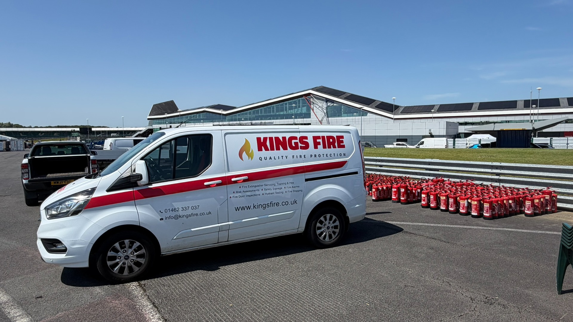 White Kings Fire service van parked beside rows of red fire extinguishers on hire at Silverstone.